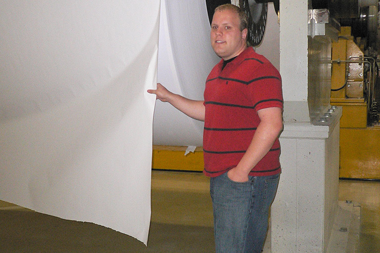 Student stands beside a large roll of paper.